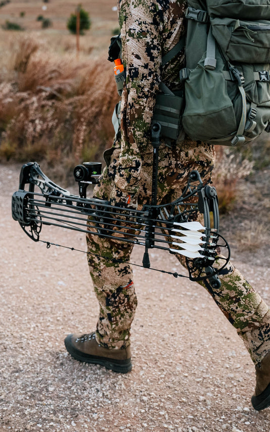 Hunter walking in SITKA Apex Collection in Optifade Subalpine and holding his Mathews Lift in Shale Gray equipped with a Bridge-Lock™ UV Slider™ and UV 1K Arrows