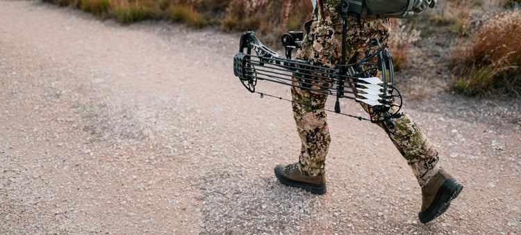 Hunter walking in SITKA Apex Collection in Optifade Subalpine and holding his Mathews Lift in Shale Gray equipped with a Bridge-Lock™ UV Slider™ and UV 1K Arrows